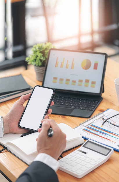 Photo cropped shot of businessman hand holding blank screeen smartphone while sitting at the table in modern office room, mock up blank screen for graphic design or product display.