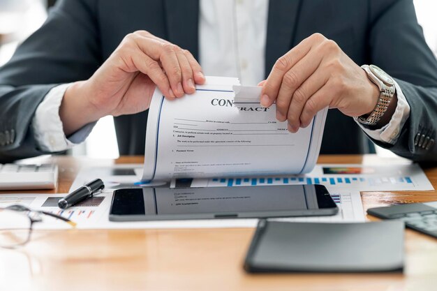 Cropped shot of businessman hand tears agreement document while
sitting at desk office, breaking contract.