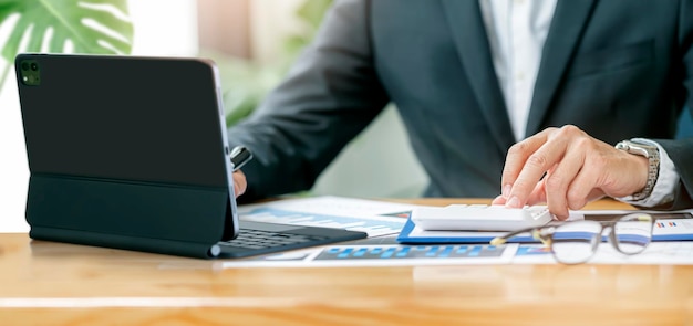 Cropped shot of businessman hands using portable tablet and calculator while sitting at the table in modern office. Business analysis and strategy concept.