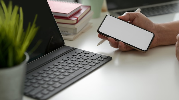 Cropped shot of businessman holding phone in modern workspace with digital tablet and office supplies