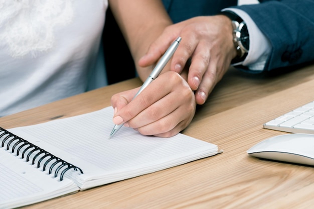 Cropped shot of businessman touching hand of young businesswoman writing in notebook