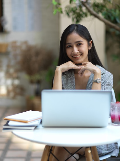 Cropped shot of businesswoman smiling to camera while working with laptop in cafe