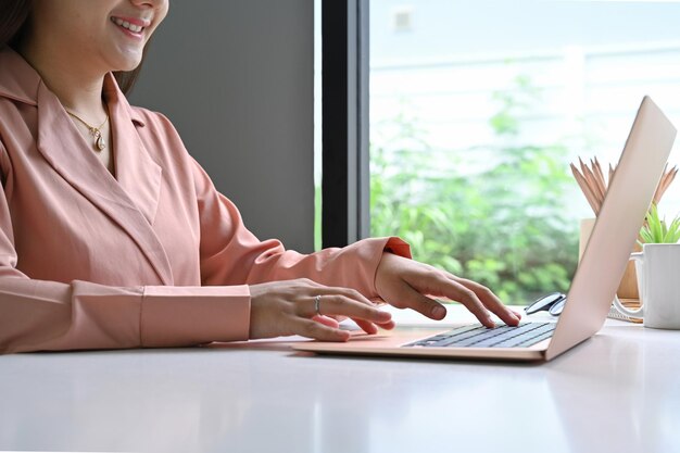 Ritagliata imprenditrice sorridente e lavorando con il computer portatile in ufficio.