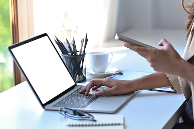 Cropped shot businesswoman working with laptop and using smart phone in office.