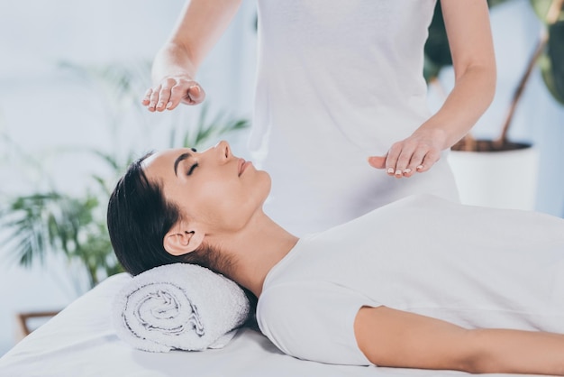 Cropped shot of calm young woman receiving reiki healing therapy on head and chest