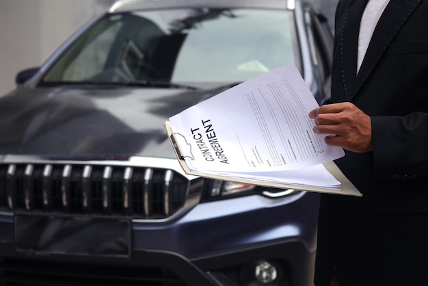 자동차 배경에 임대 문서를 들고 있는 자동차 렌탈 판매의 자른 샷.