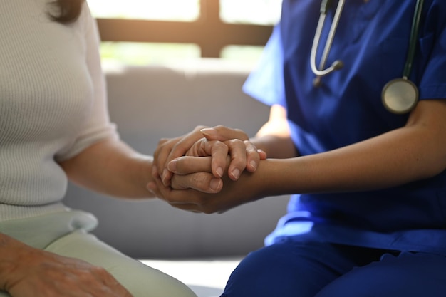 Cropped shot of caring nurse holding senior woman hands for hope and supporting Elderly healthcare concept