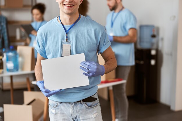 Foto ritagliata colpo di giovane volontario maschio caucasico in uniforme blu e guanti protettivi che sorride a