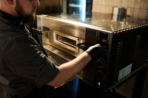 Cropped shot of chef in workwear choosing temperature of electric oven