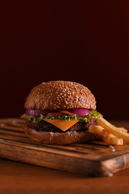 Cropped shot of delicious grilled beef burger and french fries on wooden tray on the table