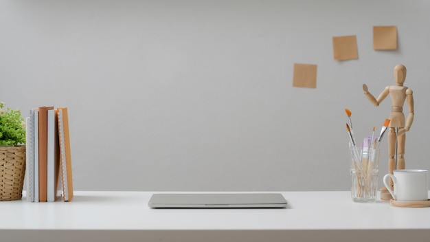 Cropped shot of designer workplace with laptop, coffee cup, painting tools and decorations on white desk