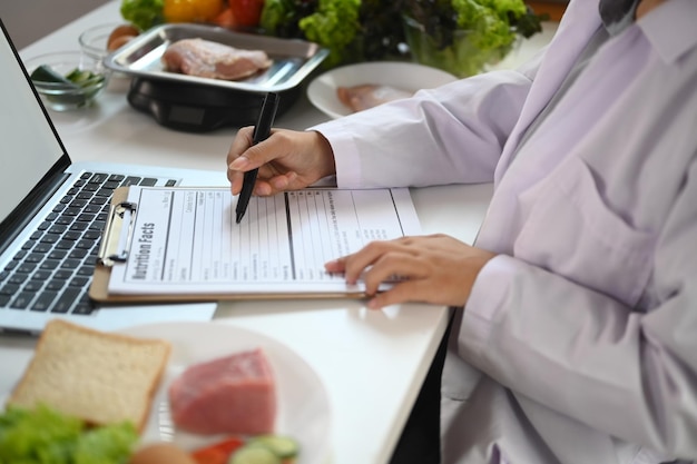 健康的な食事コンセプトを様々な健康的な製品で机で働くクロップショット栄養士