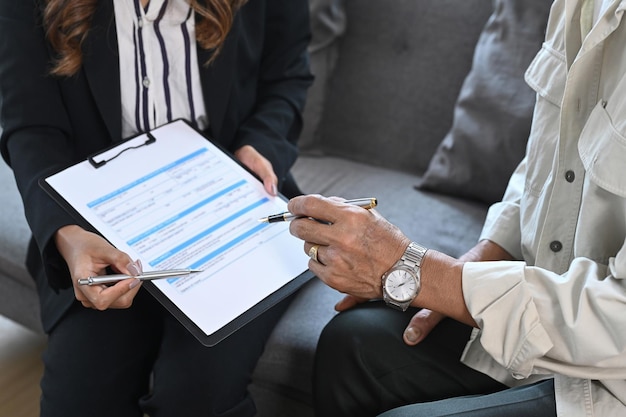 Cropped shot of elderly man sitting in insurance agency office and signing on health insurance agreement