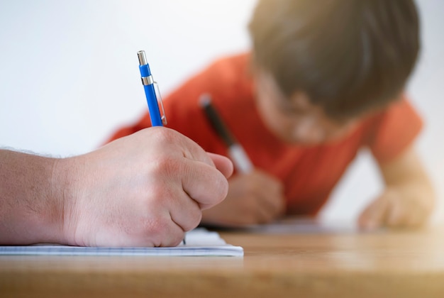 父親が宿題を手伝い、父と息子が一緒に宿題をし、教師が小さな男の子に文章を書く方法を教えているショットショットをトリミングしました。鉛筆、教育コンセプトを持っている男の手