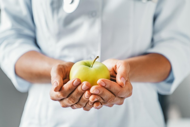 Photo cropped shot of female doctor holding apple with both hand in clinic