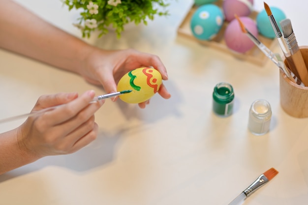 Cropped shot of female hand with paintbrush painting on egg, preparing for Easter festival