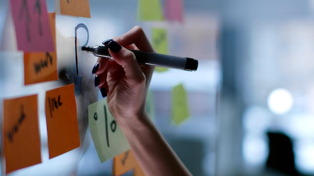 Cropped shot of female hand writing PLAN on glass board with colorful stickers in modern office