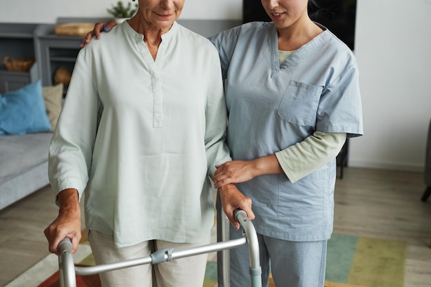 Cropped shot of female nurse helping senior woman using mobility walker in retirement home copy space