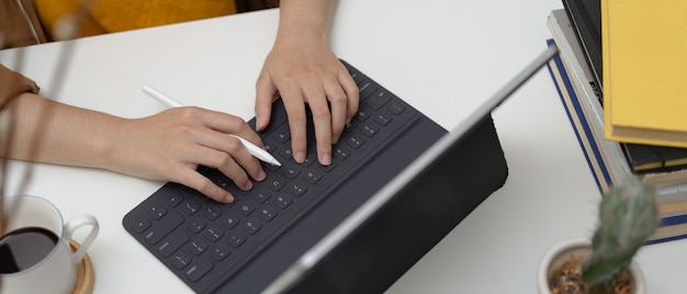 Cropped shot of female typing on tablet keyboard on worktable with coffee cup