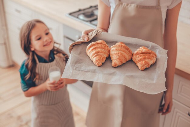 クロワッサンとトレイを保持している母親を見ている女の子のトリミングされたショット