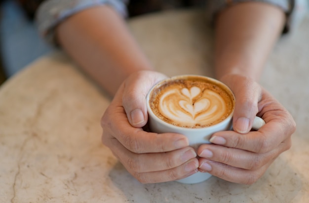 ラテコーヒーカップを持っている手のクロップドショット。