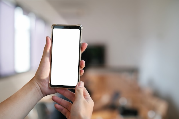 Cropped shot of hands holding smartphone with blank screen and blurred office background.