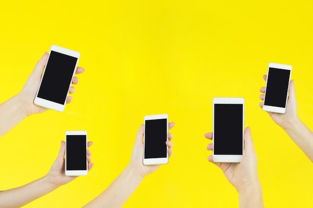 Photo cropped shot of hands holding smartphones on yellow.