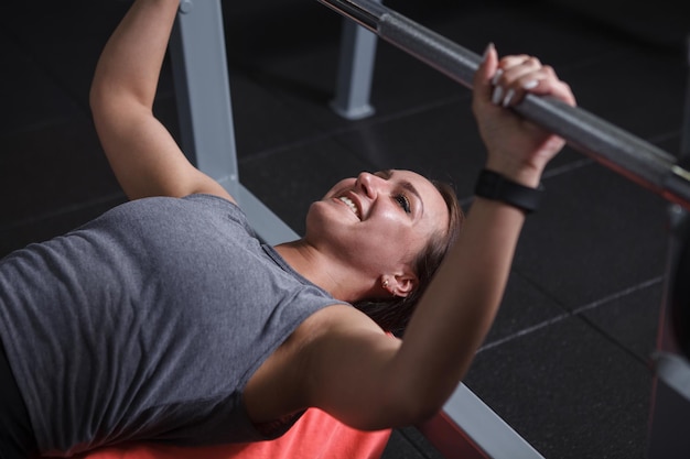 Photo cropped shot of happy healthy sportswoman smiling while doing bench press at gym