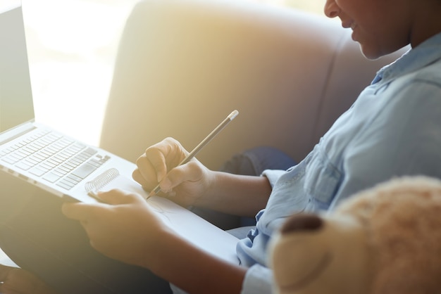 Cropped shot of happy teen schoolgirl drawing while doing homework sitting on the sofa at home