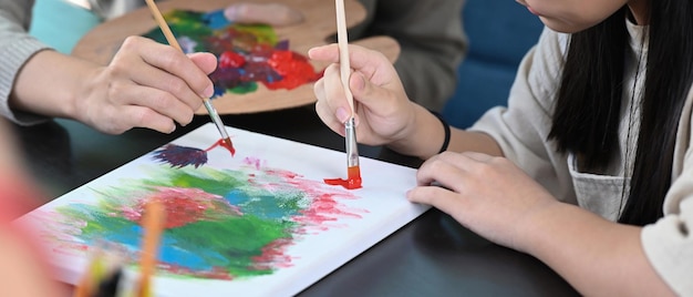 Cropped shot little girl painting picture in art class with teacher.