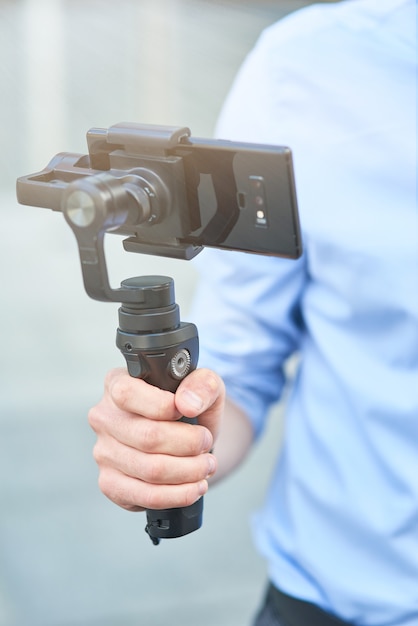 Cropped shot of a male blogger holding a gimbal with smartphone while standing outdoors recording