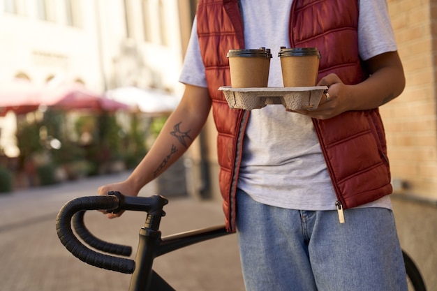 Cropped shot of a male courier delivering four coffee cups to cu