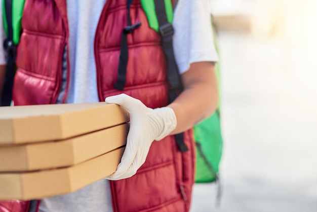 Ritagliata di un corriere maschio che indossa guanti protettivi che consegna scatole con pizza durante la pandemia di coronavirus