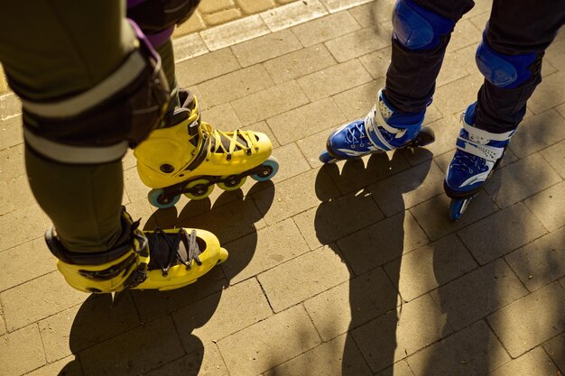 Cropped shot of man and boy legs wearing rollerblades over city park background. Active recreation time and sports activity in summer