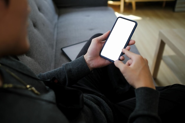 Cropped shot of man holding mock up mobile phone and sitting on couch.