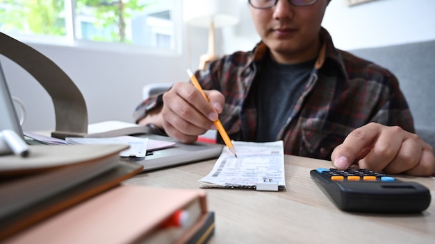 Обрезанный снимок человека с помощью калькулятора и управления домашними финансами в гостиной.
