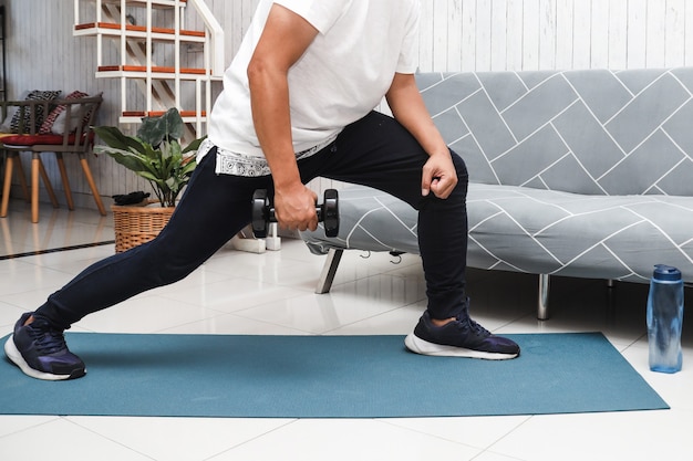 Cropped shot of a man in white shirt on blue mat lifting weight with mini dumbbells at home