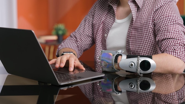 Обрезанный снимок человека с бионической рукой, работающего дома за компьютером