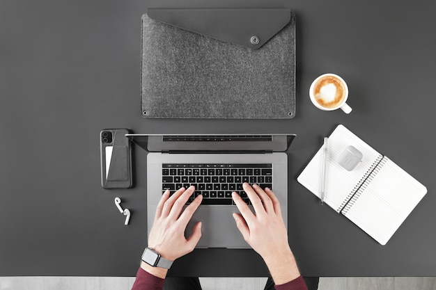 Cropped shot of man working with laptop on black table top with coffee and digital devices