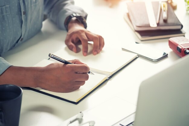 Foto ritagliata ha sparato a un uomo che scrive su carta per notebook sul posto di lavoro.