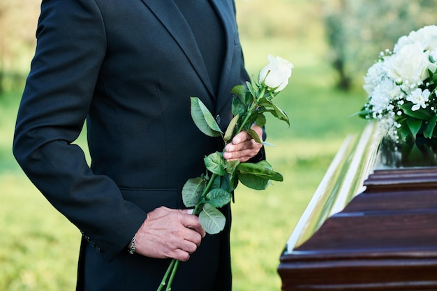 cropped shot of mature widower in black suit standing by coffin with closed lid