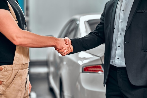 Cropped shot of a mechanic shaking hands with the car service client repaired car on the background