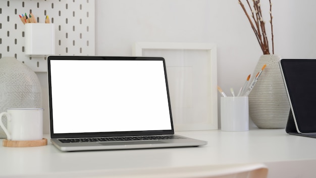 Cropped shot of minimal artist workplace with blank screen laptop, tablet , painting brush and decorations