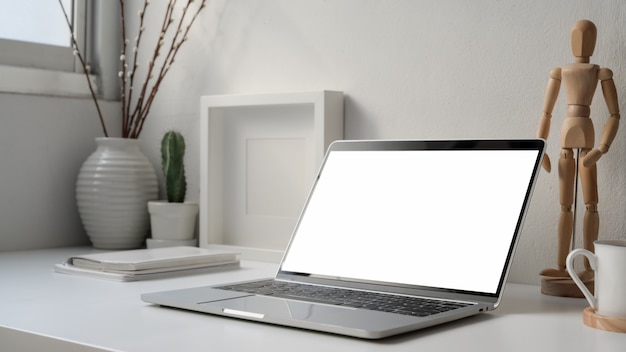 Cropped shot of minimal workplace with blank screen laptop, wooden figure and decorations