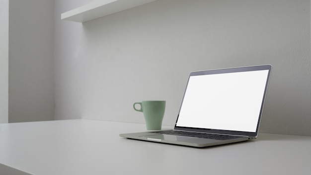 Cropped shot of minimal workspace with open blank screen laptop, mug and copy space