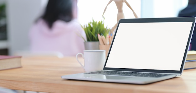 Cropped shot of modern office room with open blank screen laptop and office supplies with employees