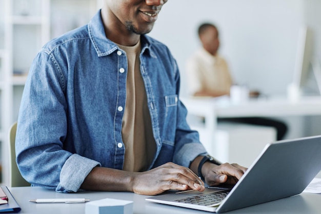 사무실에서 일하고 최소한의 회색 인테리어 카피로 노트북을 사용하는 웃고 있는 흑인 남성의 자른 사진