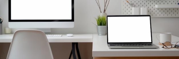 Cropped shot of office desk with computer devices, supplies and decorations on white table