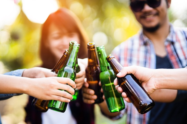 Cropped shot of people holding beer glasses celebrating in the summer camping party outdoor. Friends clinking bottle of beer during camping outdoor