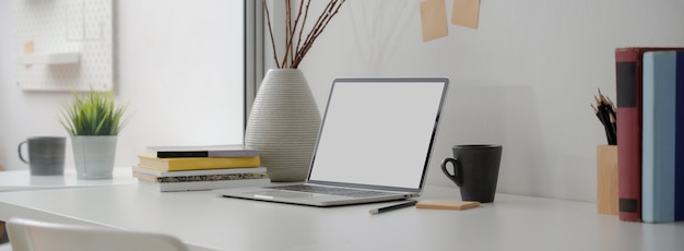 Cropped shot of portable workspace with  laptop, mug, books, notepad and decoration